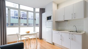 A modern kitchen with white cabinets, a microwave, and a sink. There is a dining area with a table and chairs, and a window with curtains. - OK Las Canteras 5C by CanariasGetaway (Las Palmas de Gran Canaria)