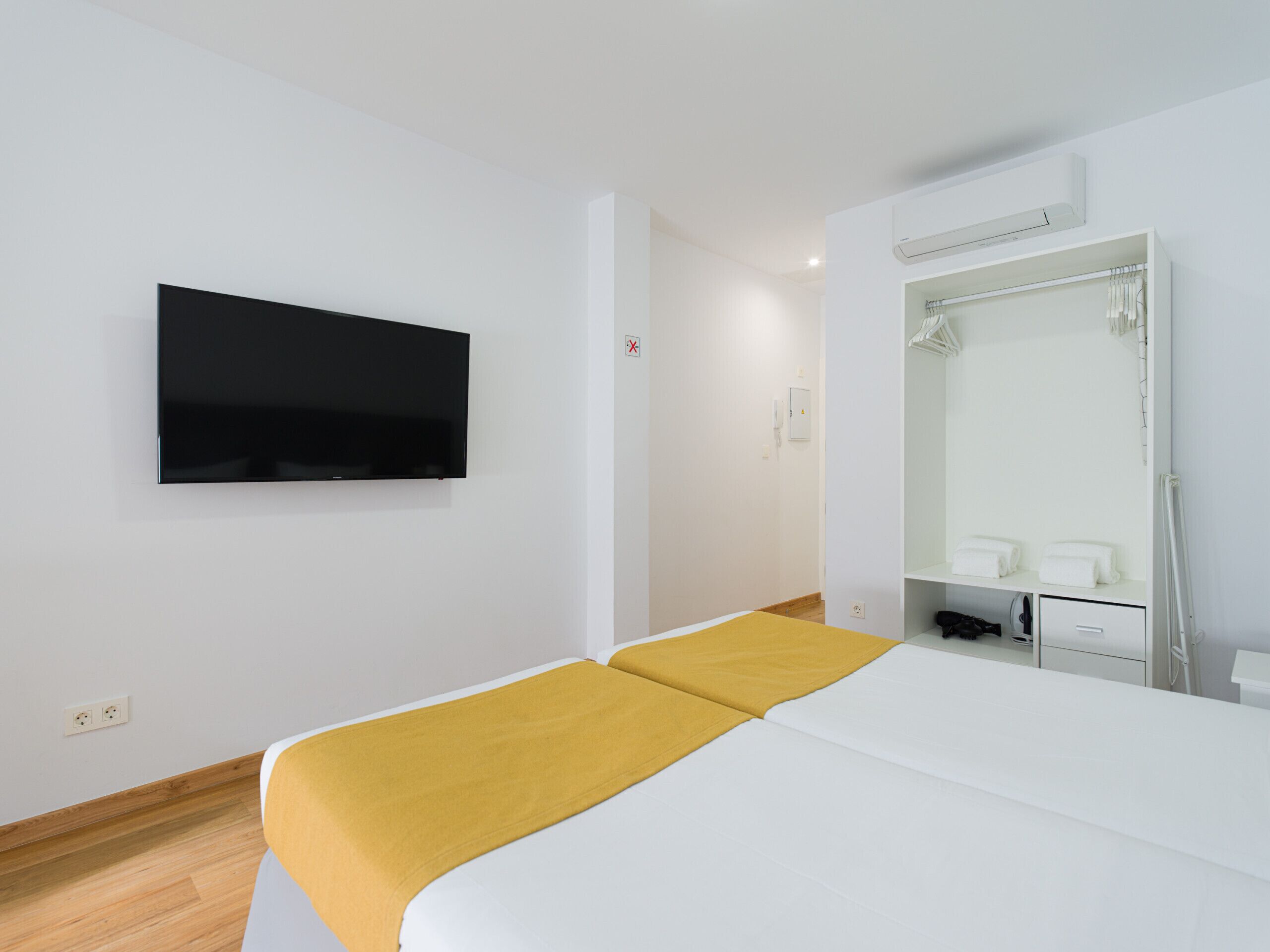 Habitación de hotel con cama, televisor montado, espejo y zona de ducha.
