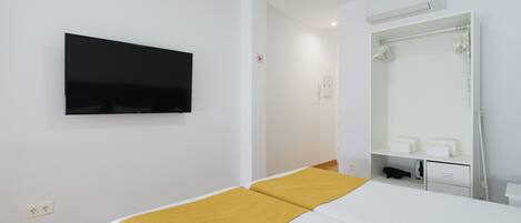 Habitación de hotel con cama, televisor montado, espejo y zona de ducha.