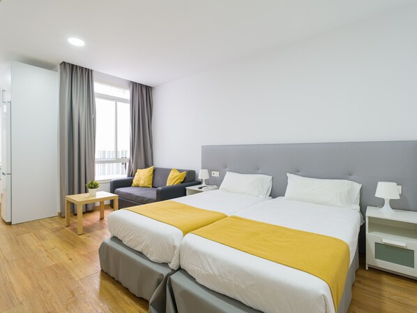 A hotel room with a double bed, a sofa, a small table, and a nightstand.