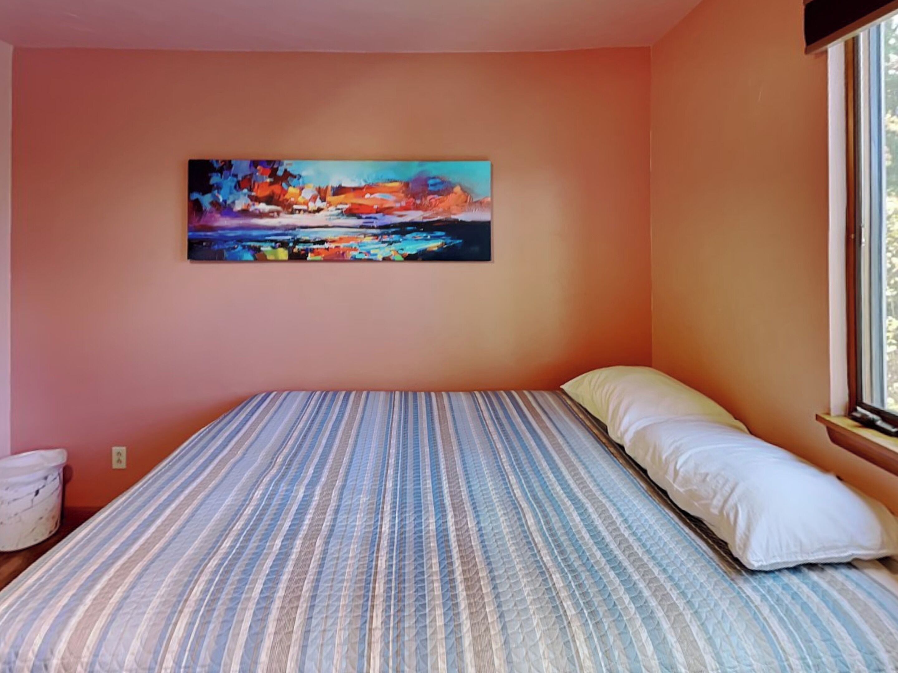 Een slaapkamer met een bed, een schilderij aan de muur en een raam.
