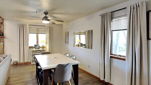 A dining area with a table, chairs, a ceiling fan, and a window with curtains.