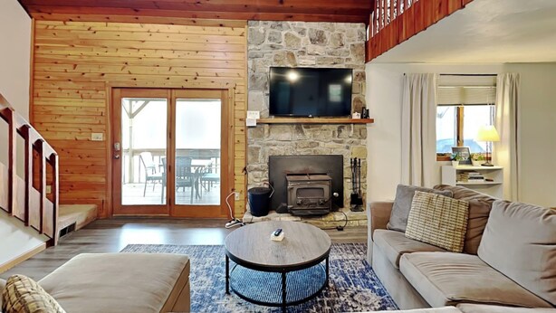 A cozy living room with a stone fireplace, wooden ceiling, and a television mounted above it.