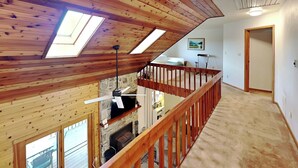 A loft bedroom with a sloped ceiling, skylights, a fireplace, and a wooden balcony railing.