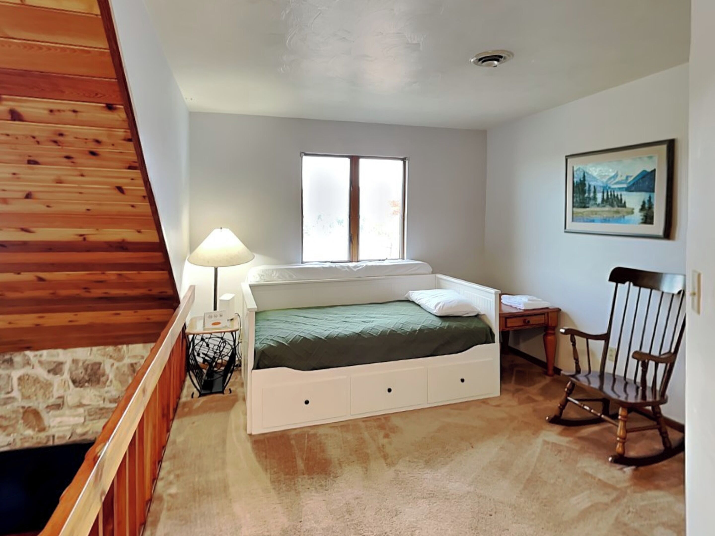 A bedroom with a bed, a window, a lamp, a chair, and a painting on the wall.