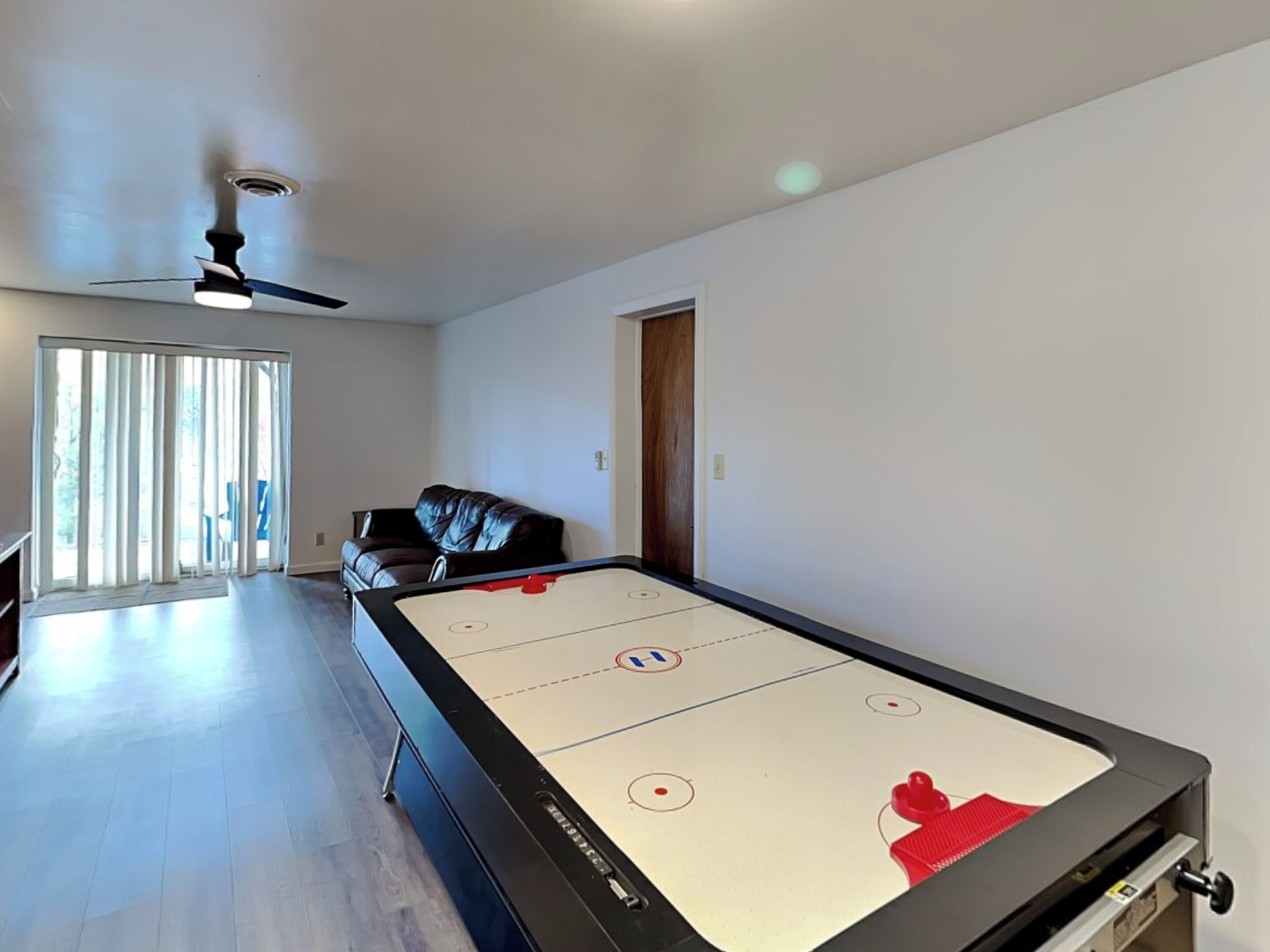 Une pièce spacieuse équipée d’une table de billard, d’un ventilateur de plafond et d’une porte-fenêtre coulissante donnant sur un patio.