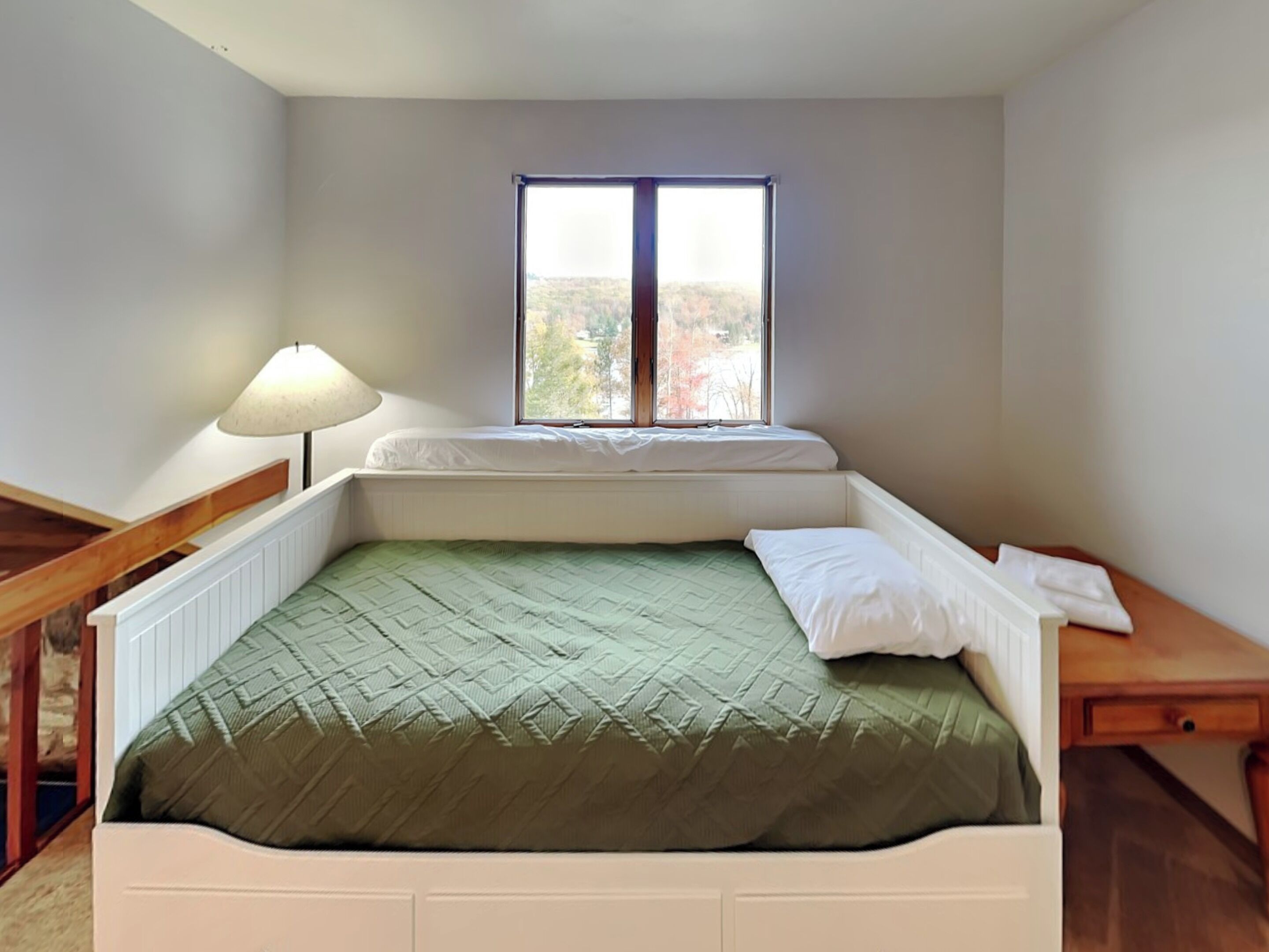 Una habitación pequeña con cama individual, ventana, mesita de noche y lámpara.