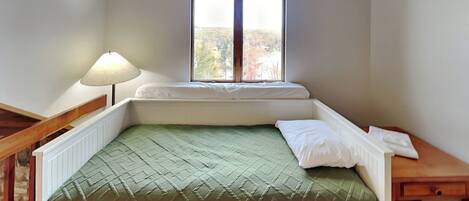 Una habitación pequeña con cama individual, ventana, mesita de noche y lámpara.