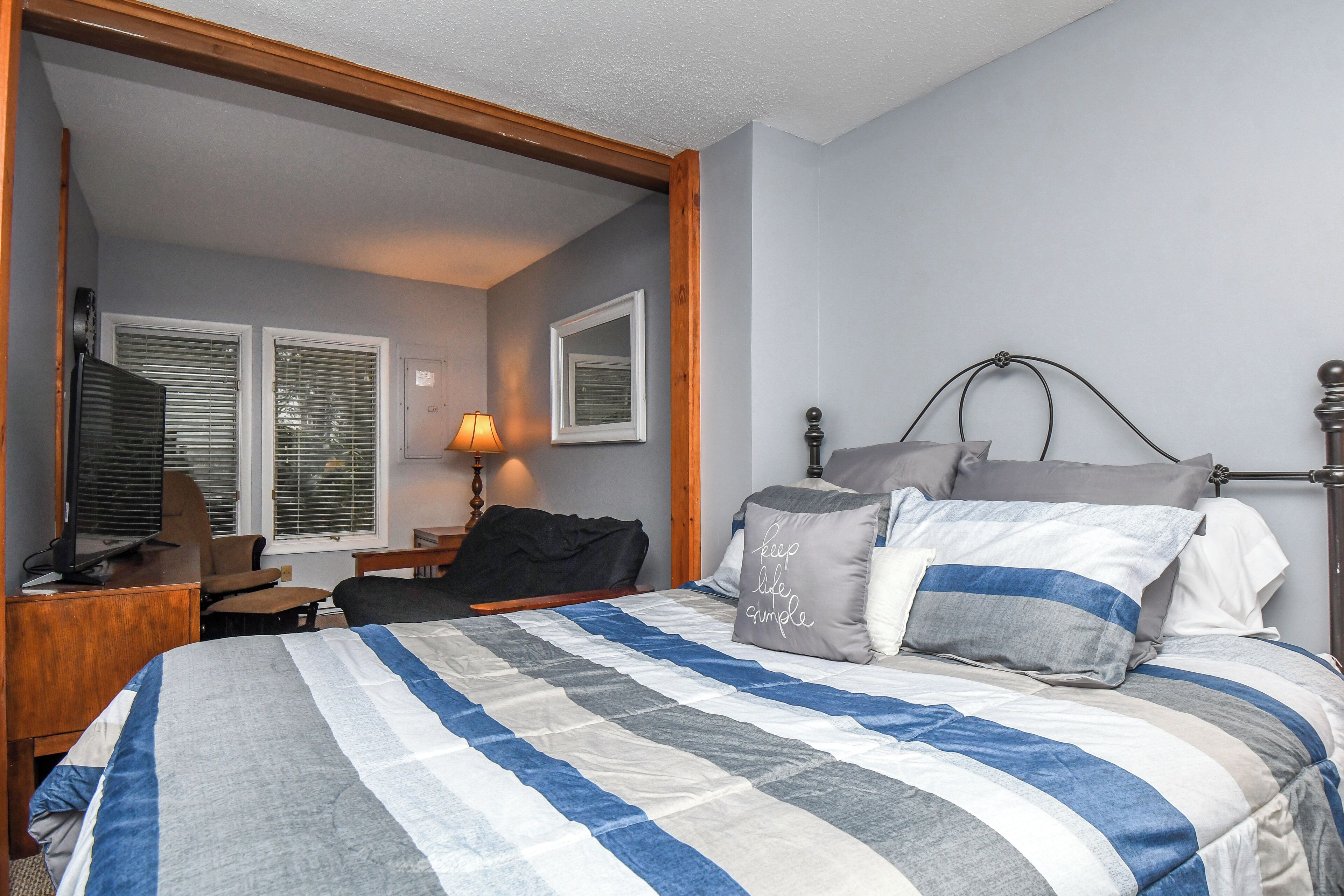 Une chambre à coucher avec un lit, un bureau avec un ordinateur, une chaise et une lampe.