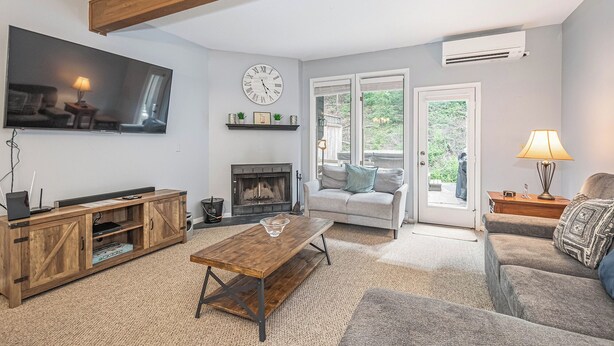 A living room with a fireplace, a television, a sofa, a coffee table, and a door leading to a balcony. - Villages of Wisp 08 Winding Way by Taylor Made Deep Creek (McHenry)