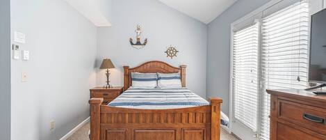 A bedroom with a wooden bed, a nightstand, a lamp, a wall clock, and a window with blinds.