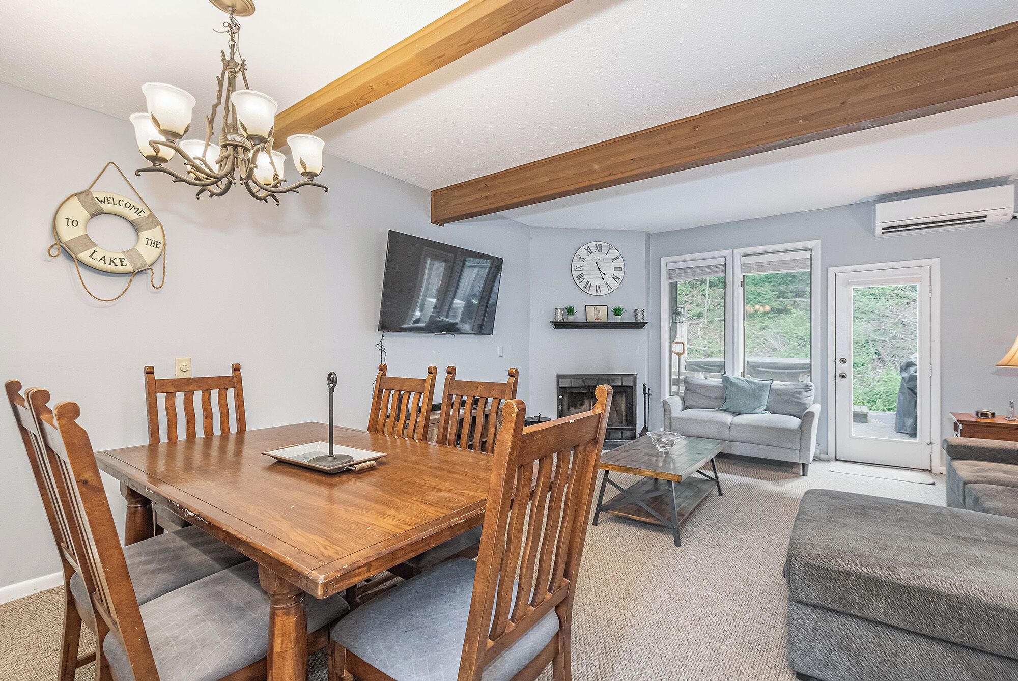 A dining area with a wooden table and chairs, a chandelier, a fireplace, a sofa, and a TV mounted on the wall.