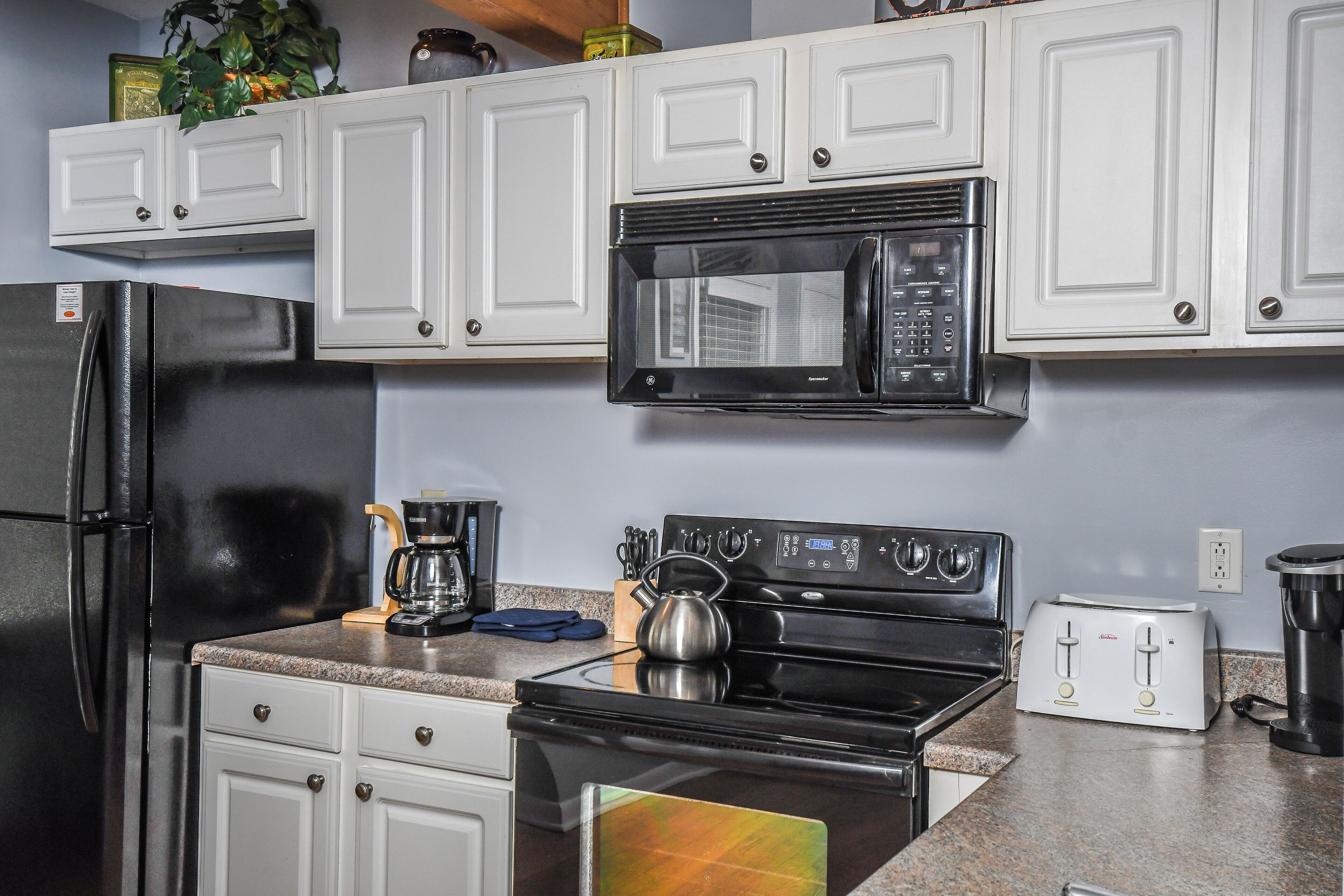 A kitchen with white cabinets, a black refrigerator, a microwave, a stove, and a toaster.