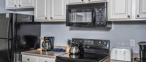 A kitchen with white cabinets, a black refrigerator, a microwave, a stove, and a toaster.