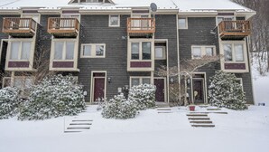 A multi-story building with balconies, a snow-covered roof, and a front entrance with steps leading up to the door. - Villages of Wisp 08 Winding Way by Taylor Made Deep Creek (McHenry)