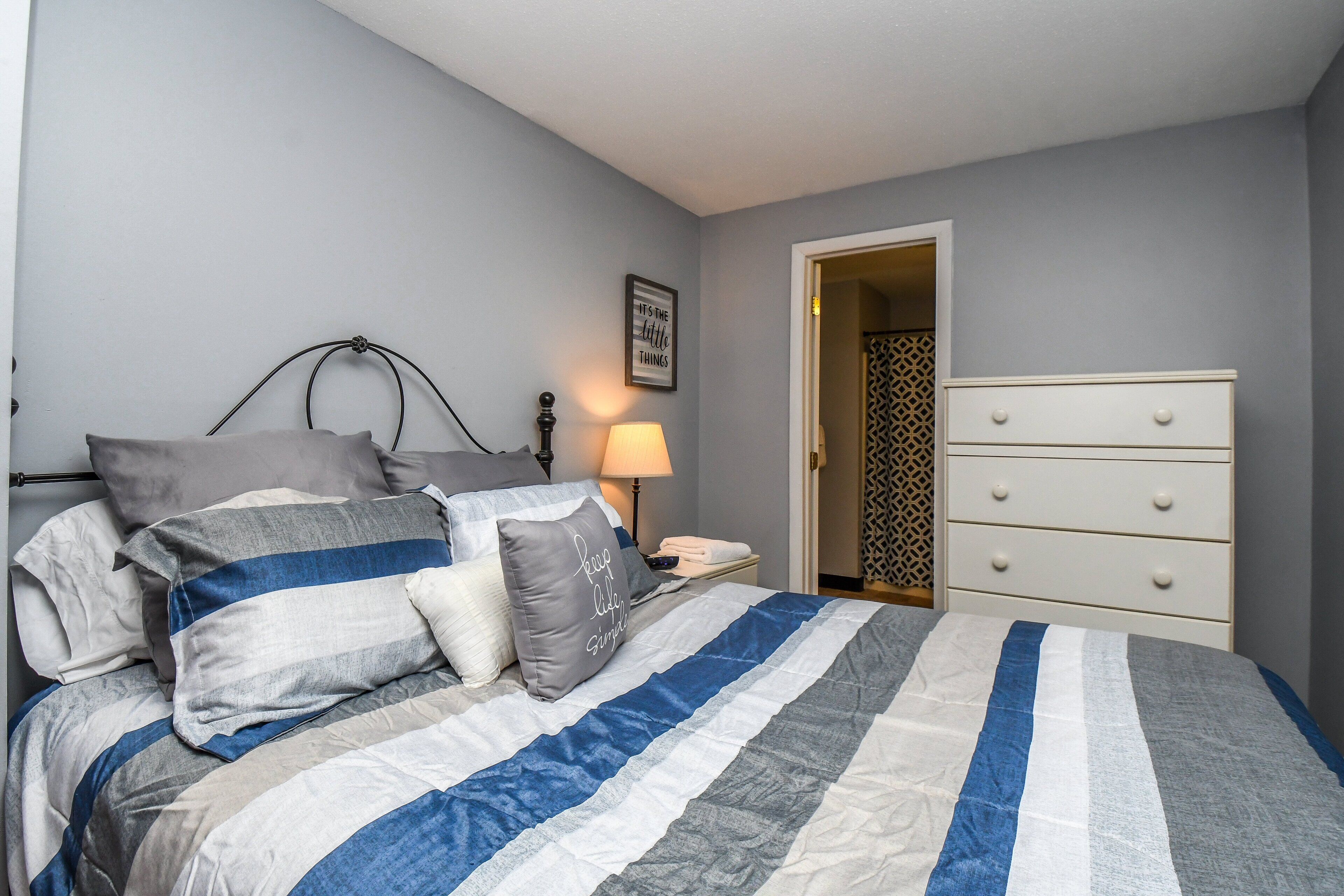A bedroom with a bed, pillows, a nightstand, a lamp, and a dresser.