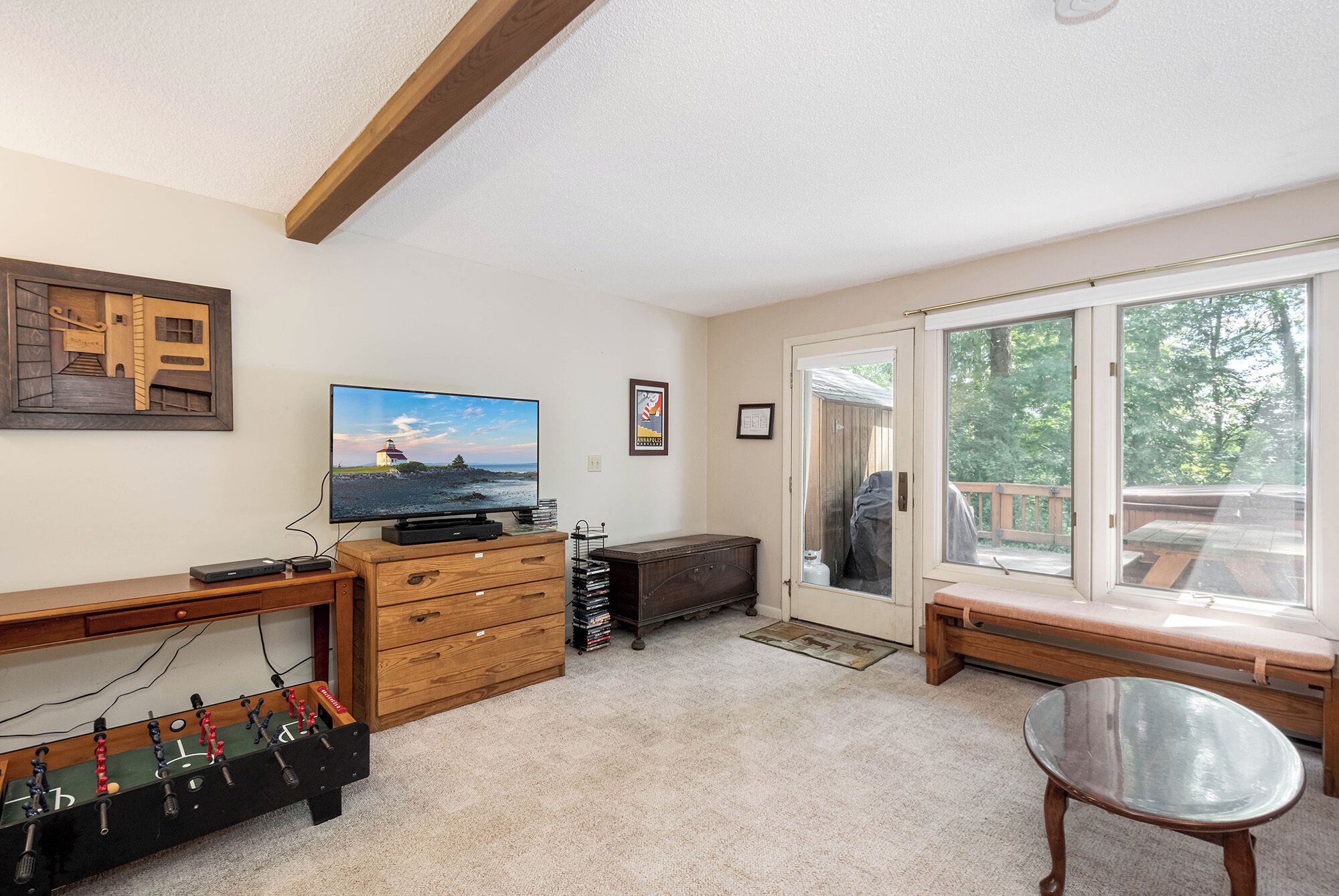 A room with a television, wooden furniture, a window with a view, and a door leading outside.