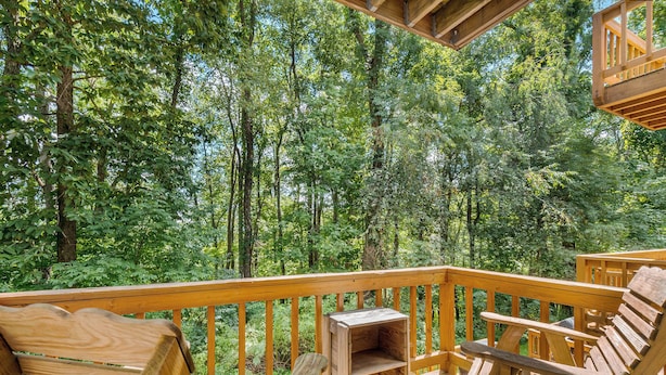 Um deck de madeira com cadeiras Adirondack e um pequeno banco de madeira, rodeado por uma floresta densa.
