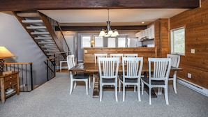 A dining area with a wooden table and chairs, a staircase, and a kitchen in the background. - Pivots & Divots by Taylor Made Deep Creek (McHenry)
