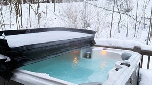 A hot tub with a snow-covered deck and surrounding trees. - Pivots & Divots by Taylor Made Deep Creek (McHenry)