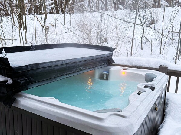 Ein Whirlpool mit einer mit Schnee bedeckten Terrasse und umliegenden Bäumen.
