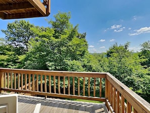 A wooden deck with a railing, surrounded by lush green trees and a clear blue sky. - Villages of Wisp 70 Bright Passage by Taylor Made Deep Creek (McHenry)