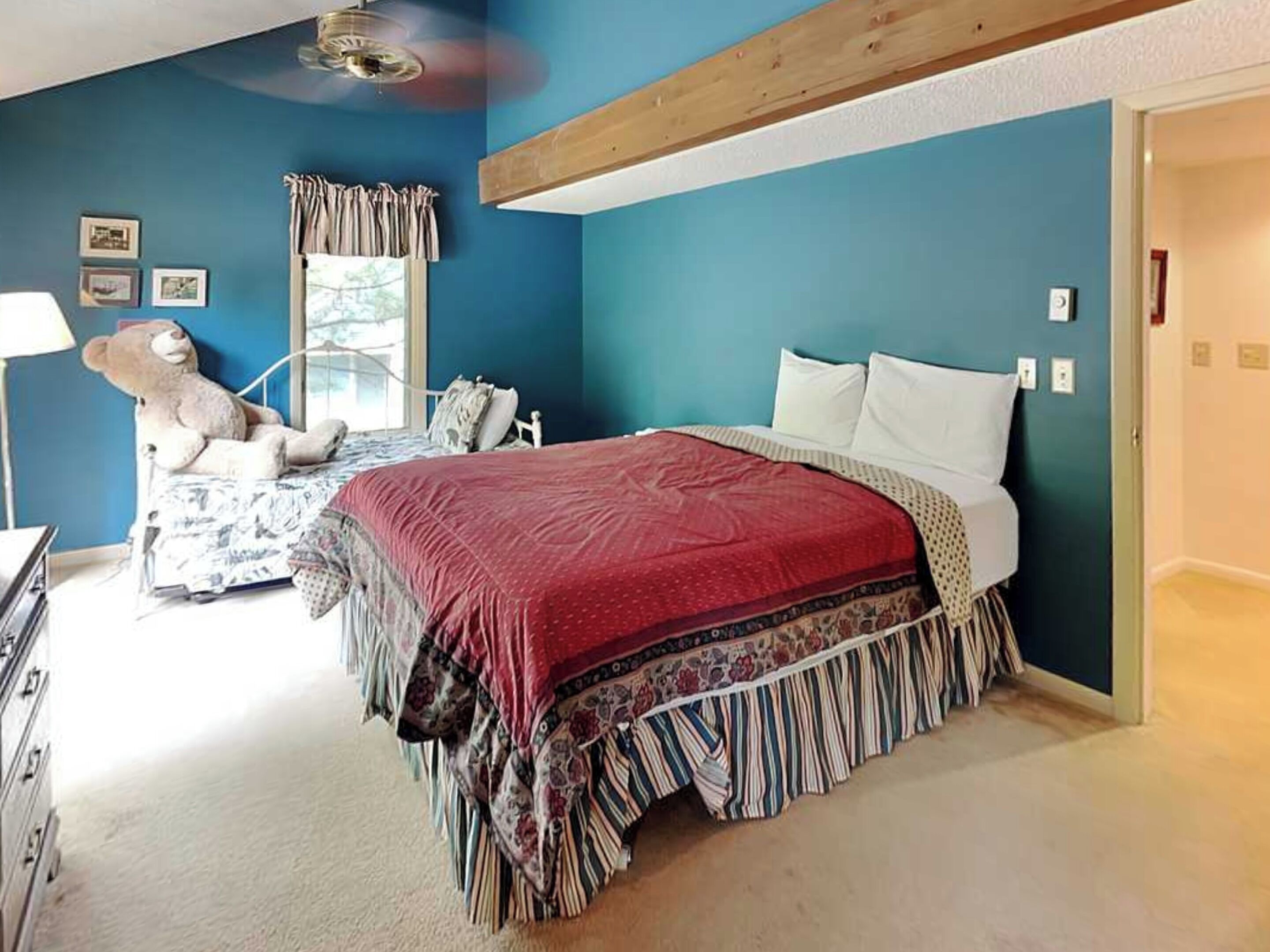 A bedroom with a bed, a chair, a window with curtains, and a ceiling fan.