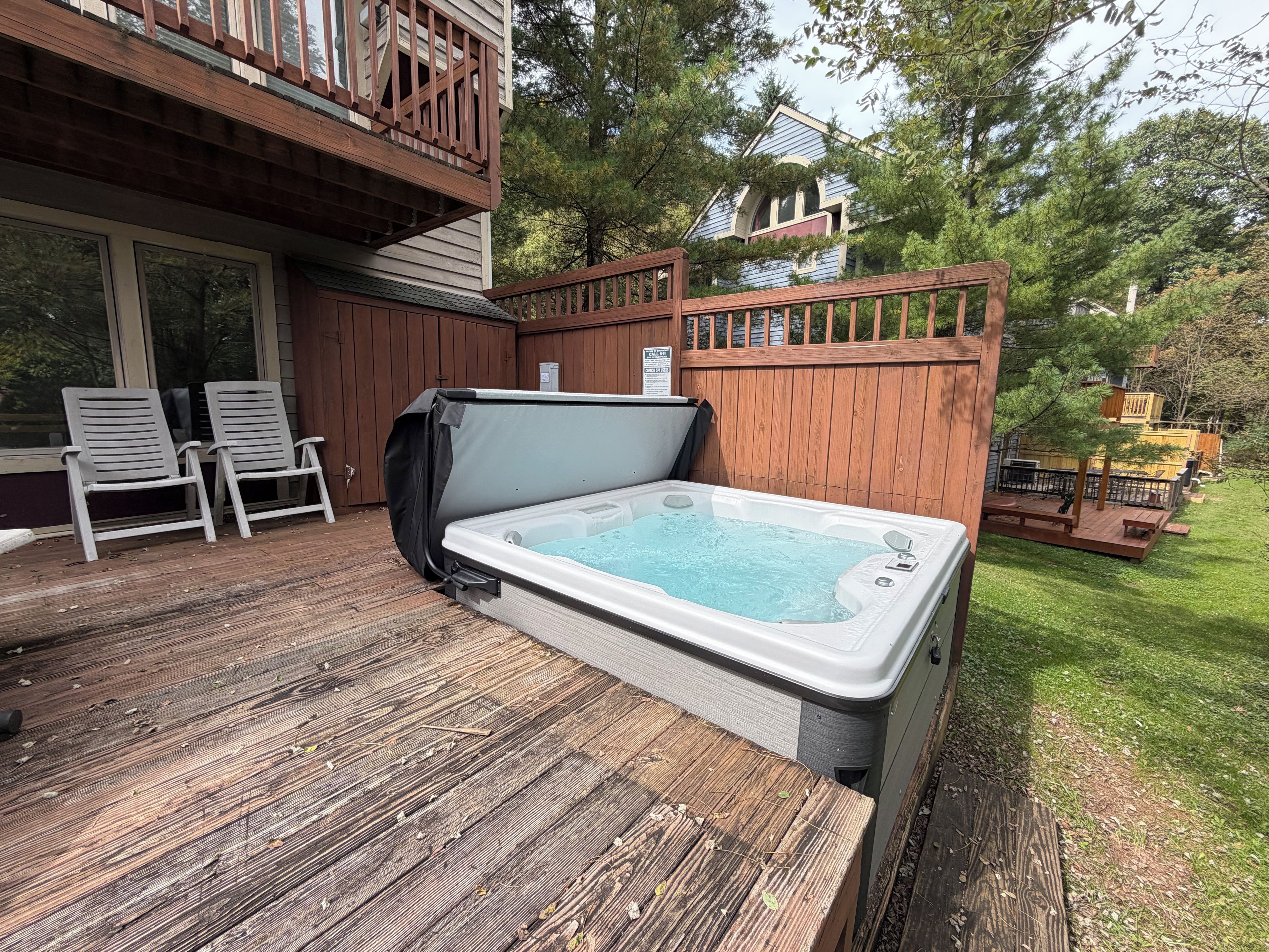 Un bain à remous sur une terrasse en bois, avec deux chaises et une table couverte à proximité.