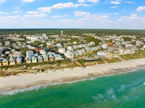 An aerial view of a coastal town with beachfront properties, a pier, and a water tower in the distance.