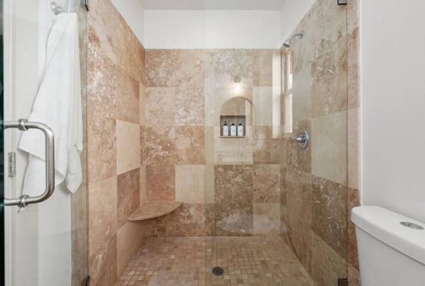 A shower area with a tiled floor, a bench, and a shelf with toiletries.