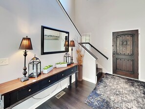 A modern entryway with a wooden console table, two wall-mounted lamps, a mirror, and a patterned rug.