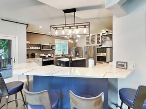 A modern kitchen with a central island, bar stools, stainless steel appliances, and a hanging light fixture.