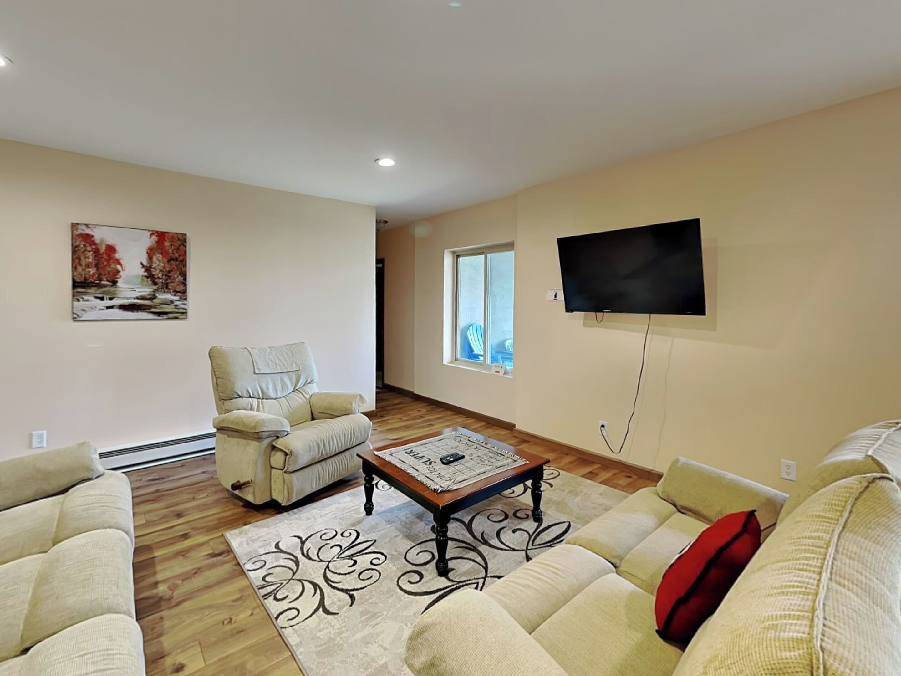 A living room with a beige sofa, a recliner, a coffee table, and a flat-screen TV mounted on the wall.