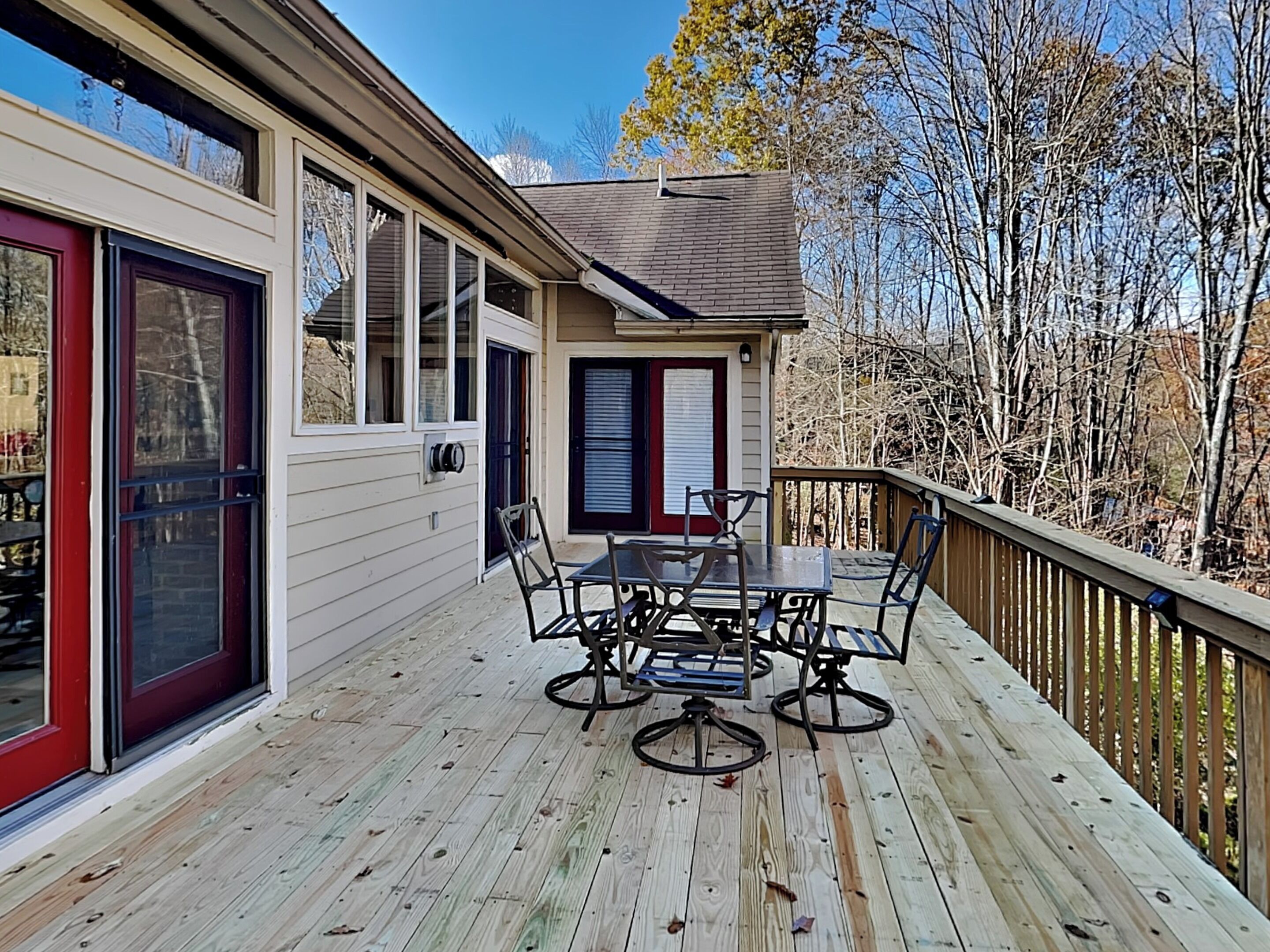 A wooden deck with a table and chairs, a sliding glass door, and a view of trees and mountains.