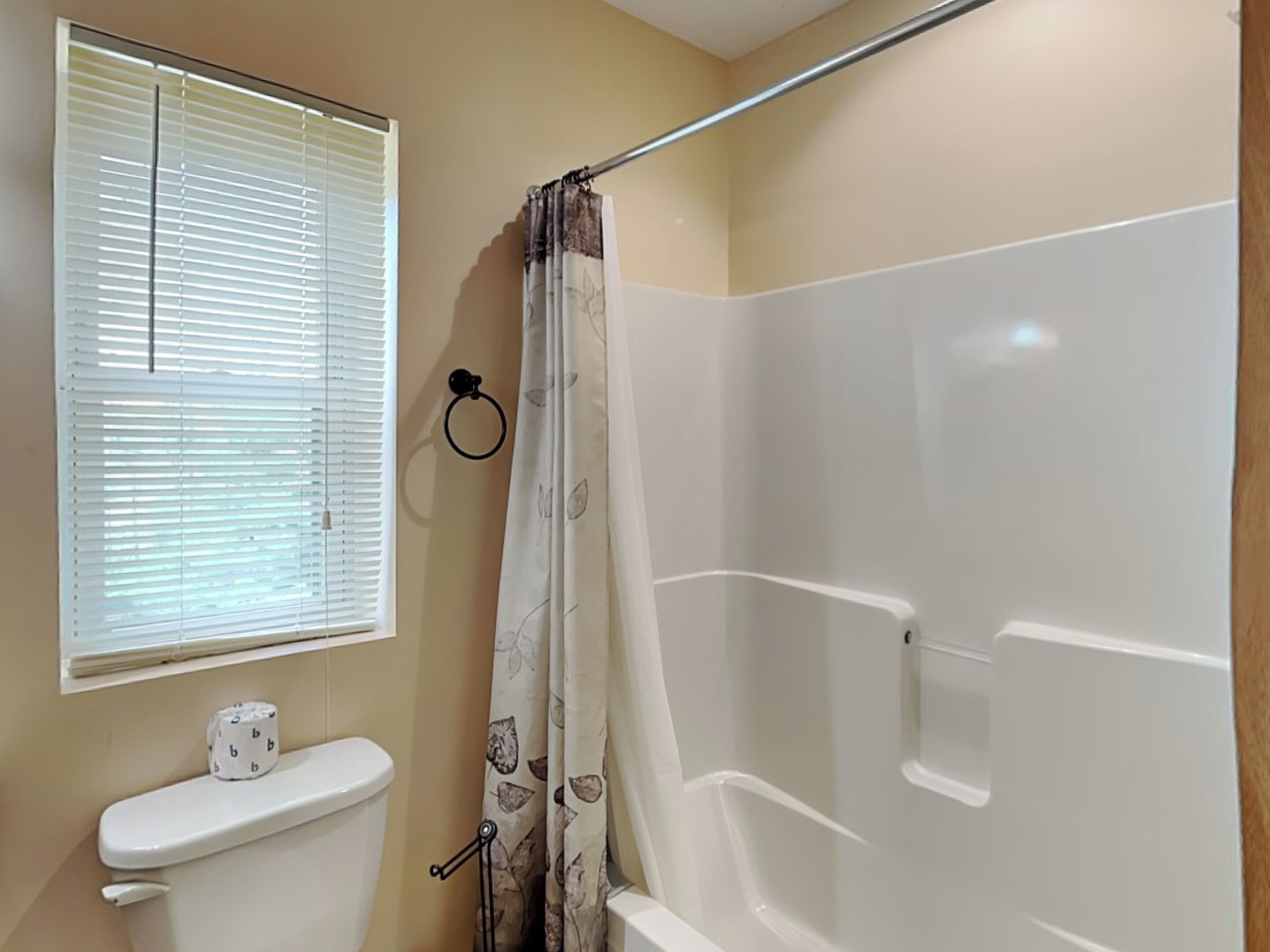 A bathroom with a toilet, a shower, and a window with blinds.