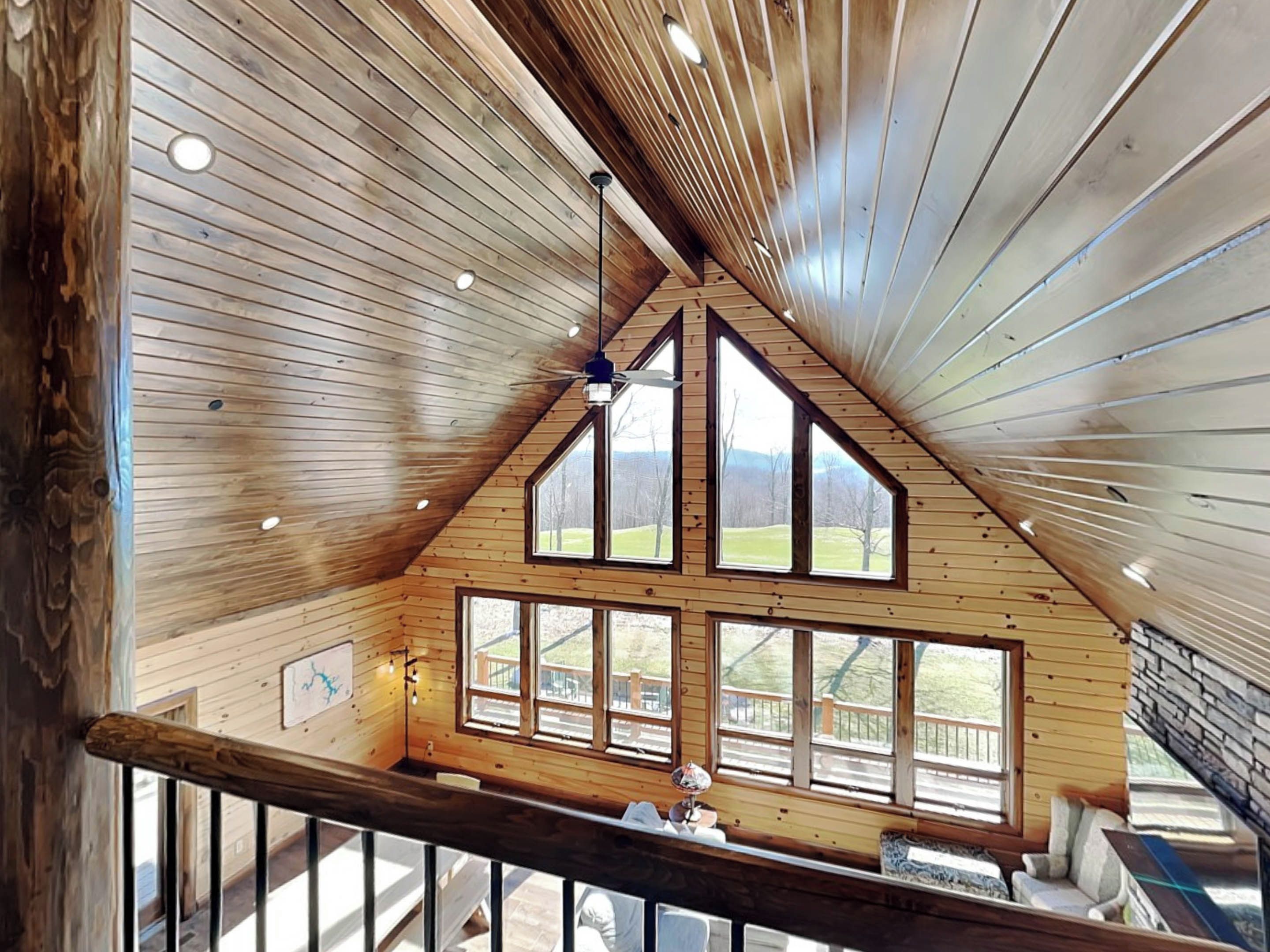 Ein Zimmer mit hohen Decken, Holzvertäfelung, großen Fenstern und Blick auf eine grüne Landschaft.