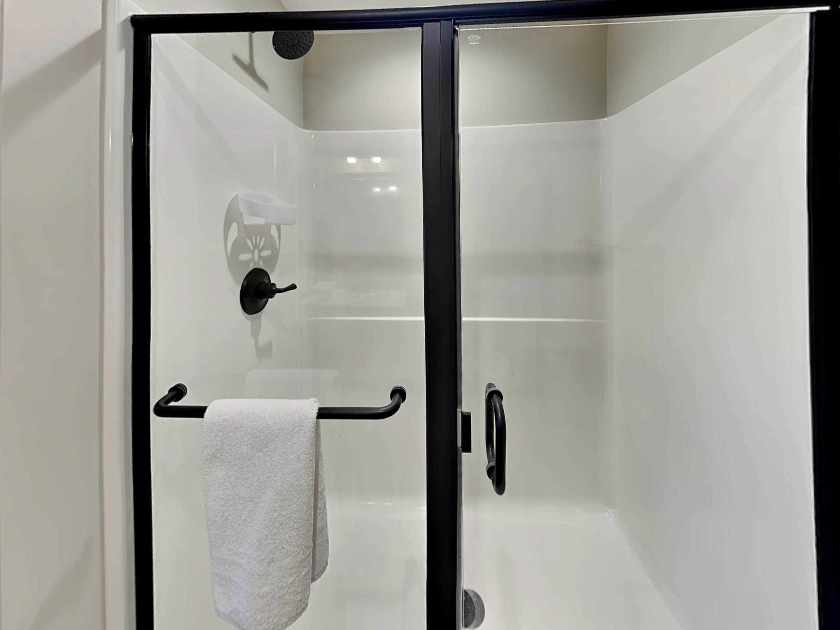 Een moderne douche met een glazen deur, een handdoekhouder en een handdouche.