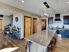 A spacious kitchen with a large island, wooden flooring, and modern cabinetry. - Water & Mountain Retreat by Taylor Made Deep Creek (McHenry)