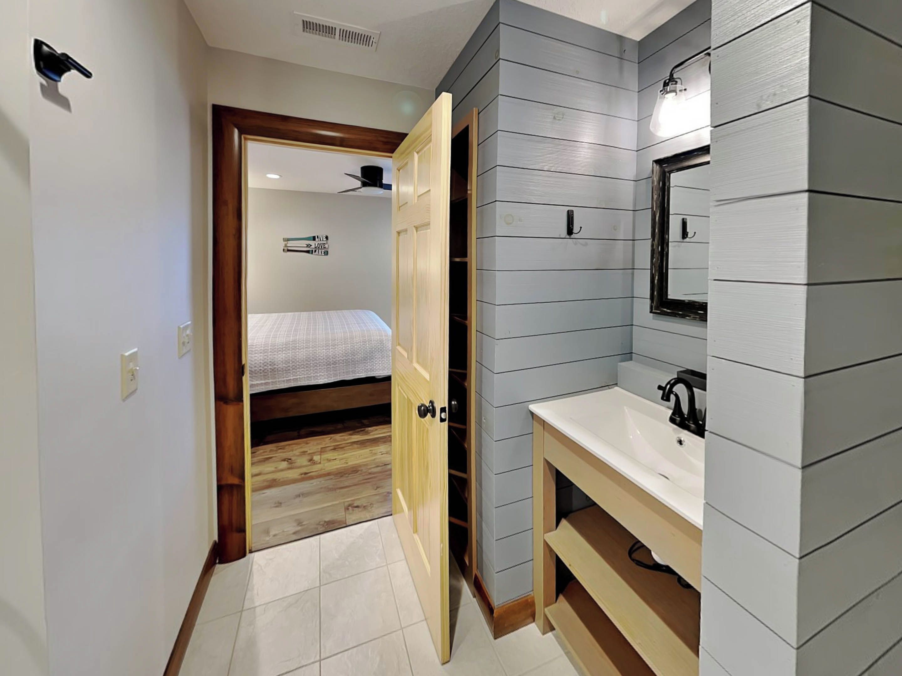 A narrow hallway leading to a bedroom with a bed and a wooden floor. A bathroom with a sink and mirror is visible to the right.