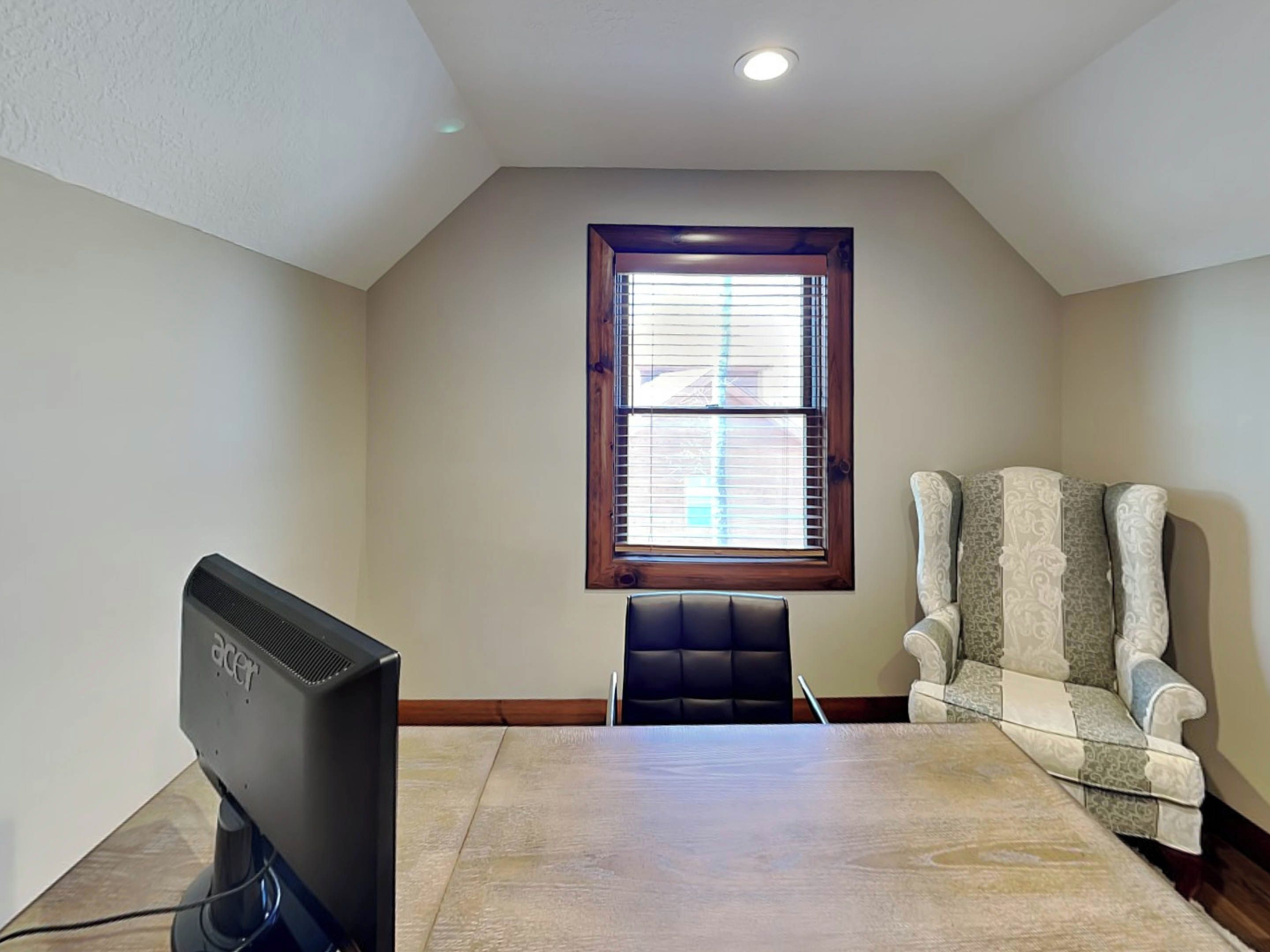 A room with a large window, a flat-screen TV, a black chair, and a patterned armchair.