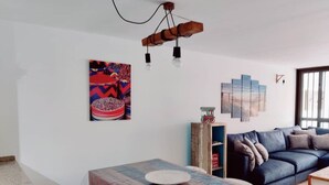 Un salon avec un canapé bleu, une table à manger en bois avec des chaises et un luminaire fixé au mur.