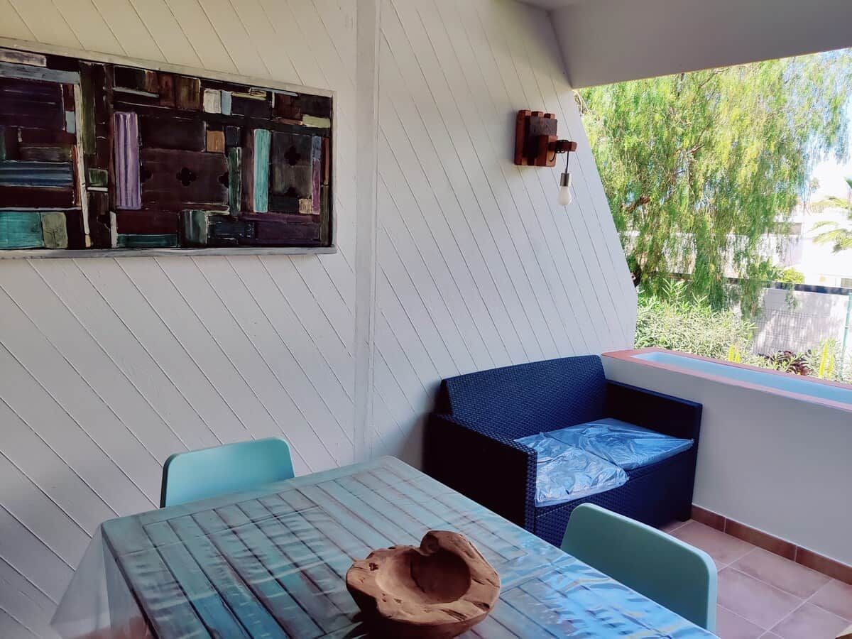 A room with a table, chairs, a sofa, a decorative wall, and a window with a view of greenery.