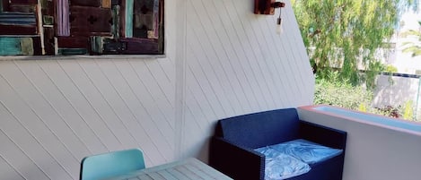 A room with a table, chairs, a sofa, a decorative wall, and a window with a view of greenery.