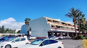 Un hotel de varios pisos con un estacionamiento lleno de automóviles, cielo azul despejado y palmeras.