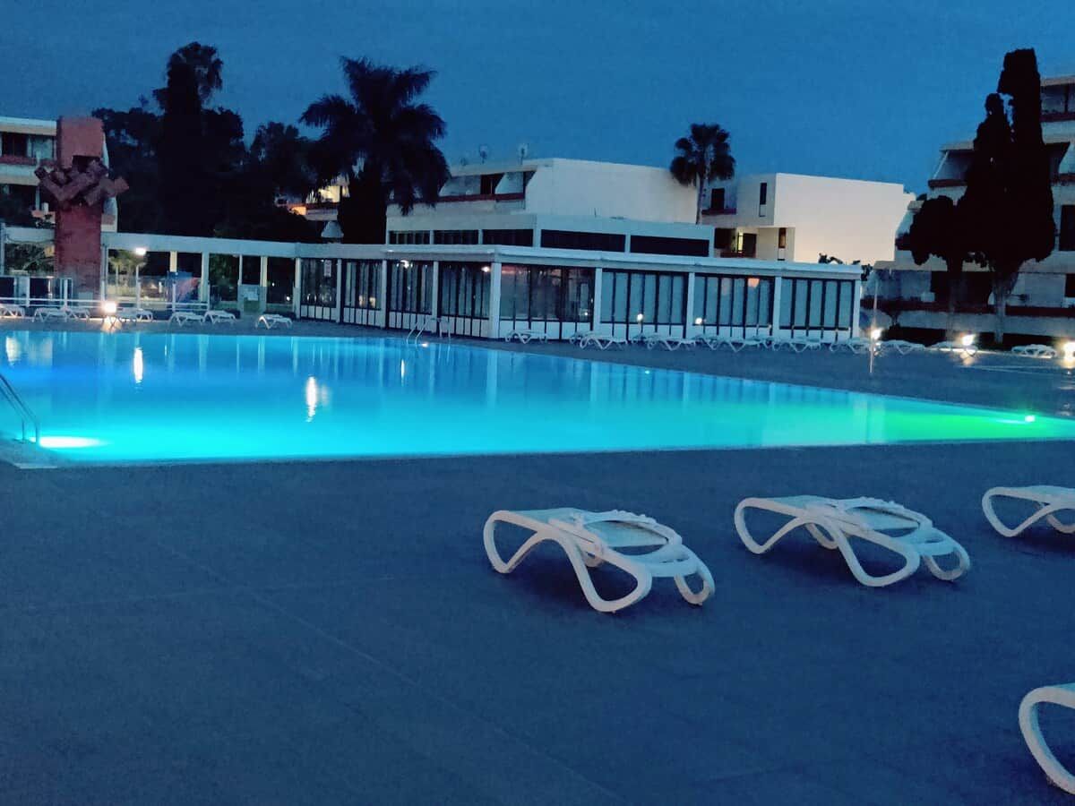 Una piscina con sillas de descanso y un edificio al fondo.