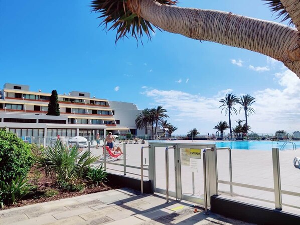 A hotel with a pool area, palm trees, and a clear sky.