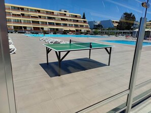 Une table de billard dans un espace extérieur ensoleillé, avec un bâtiment en arrière-plan.