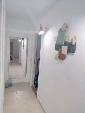 Un couloir avec un miroir, un luminaire au plafond et une œuvre d’art abstraite accrochée au mur.