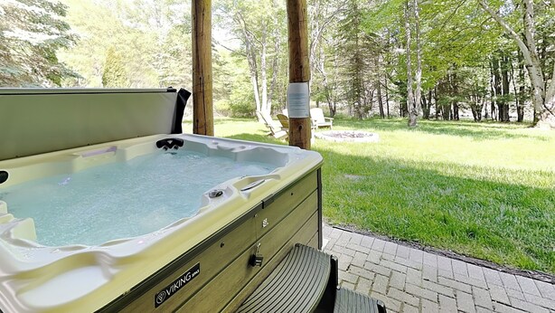 A hot tub under a wooden pergola with a grassy yard and trees in the background. - Wild Wild West by Taylor Made Deep Creek (Swanton)