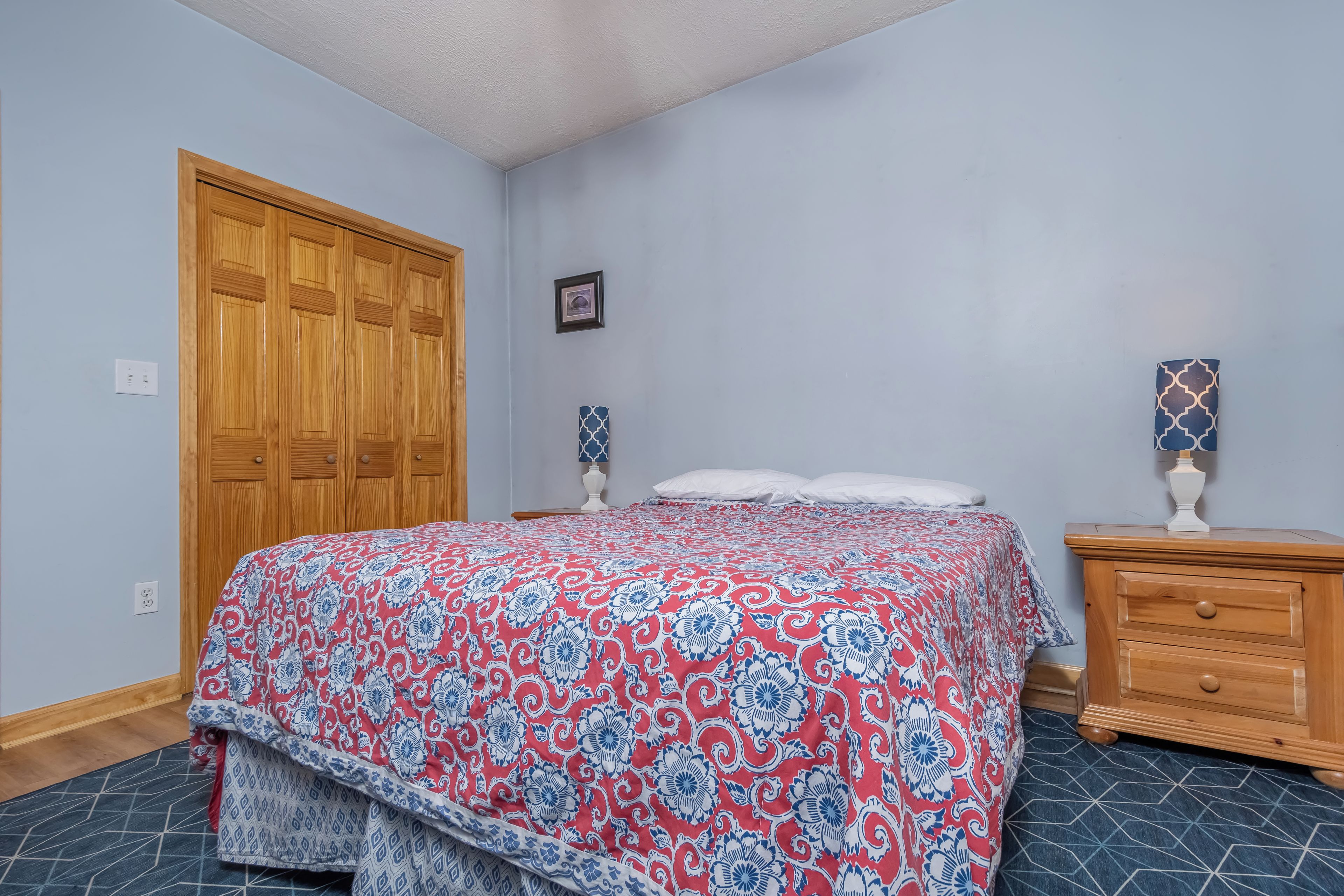 A bedroom with a large bed, wooden wardrobe, and a nightstand.